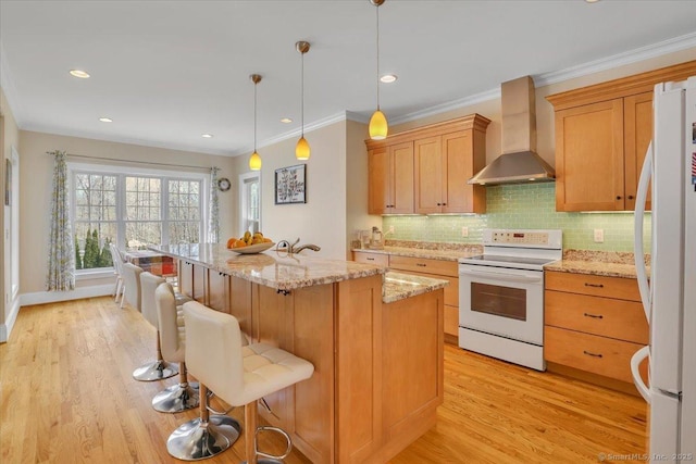 kitchen with white appliances, wall chimney range hood, light wood finished floors, light stone countertops, and a breakfast bar