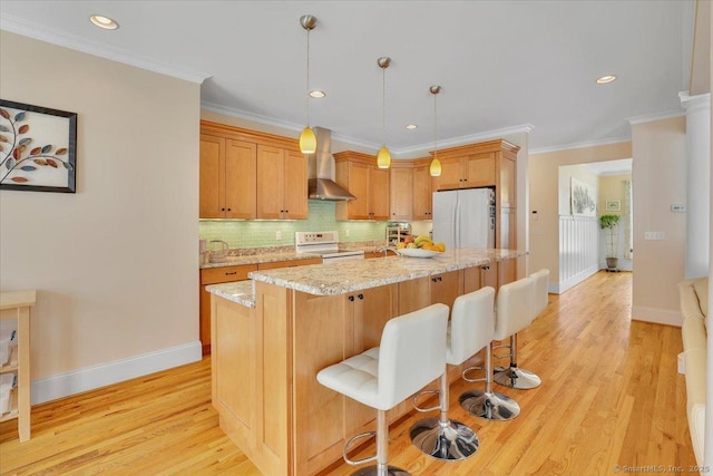 kitchen featuring white appliances, wall chimney exhaust hood, baseboards, light wood-style flooring, and crown molding