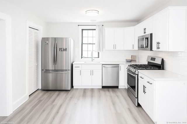 kitchen with tasteful backsplash, stainless steel appliances, light countertops, a sink, and light wood-type flooring