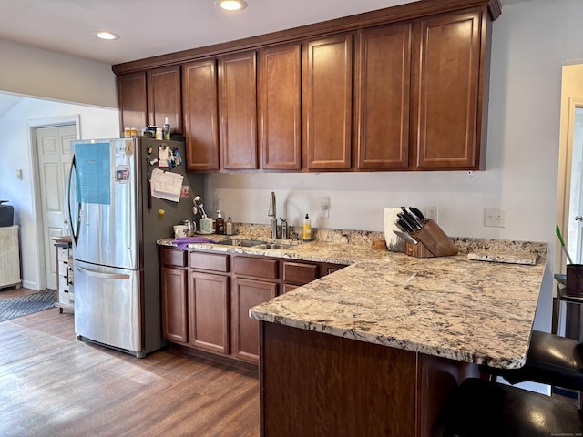 kitchen featuring a sink, a peninsula, freestanding refrigerator, light wood-type flooring, and a kitchen bar
