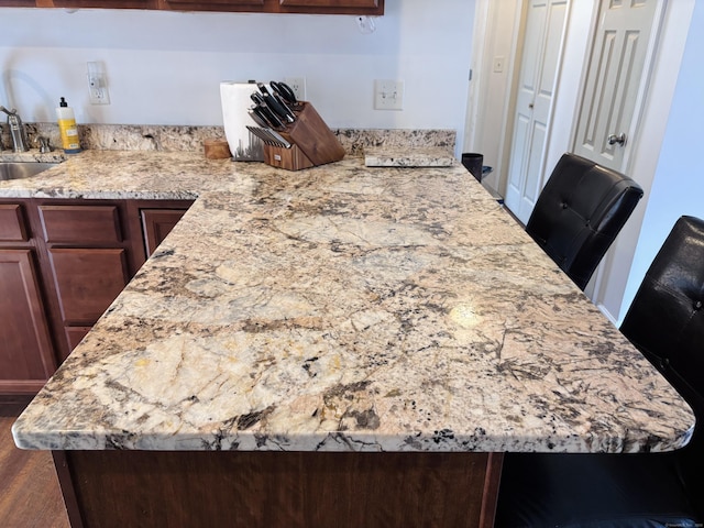 kitchen featuring dark wood-style flooring, light stone countertops, and a sink