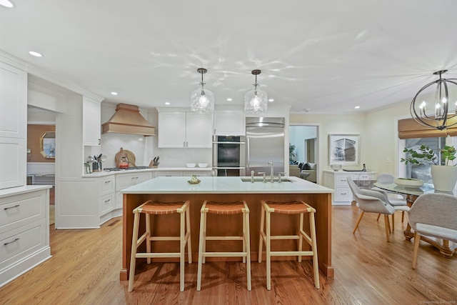 kitchen with custom range hood, stainless steel appliances, a sink, light countertops, and a chandelier