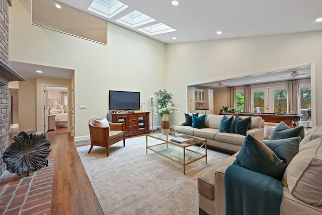living room with a skylight, a towering ceiling, recessed lighting, wood finished floors, and baseboards