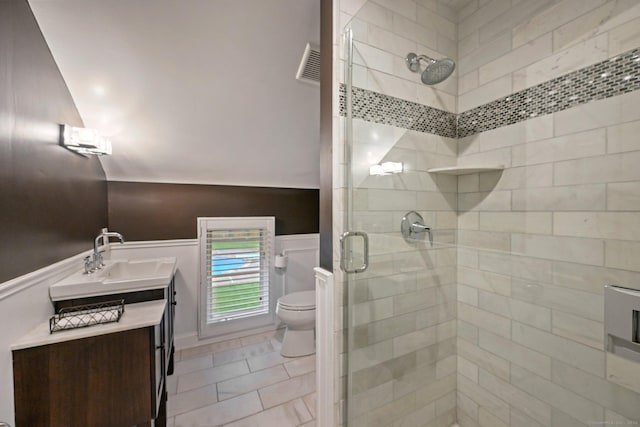full bath with a stall shower, toilet, vanity, wainscoting, and tile patterned floors