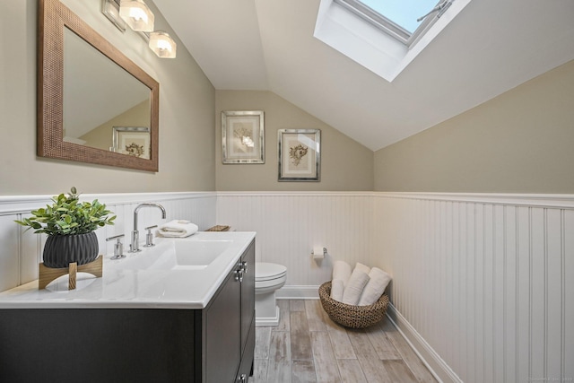 half bathroom with lofted ceiling, wood finished floors, toilet, a skylight, and wainscoting