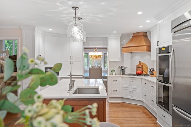 kitchen featuring custom range hood, a sink, white cabinets, a chandelier, and hanging light fixtures