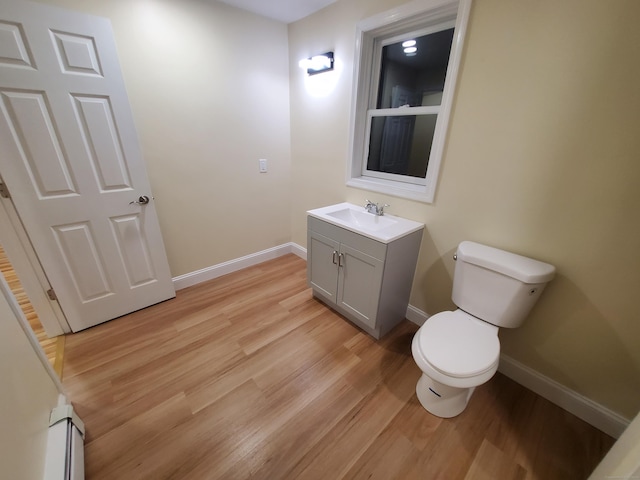 half bath featuring baseboards, wood finished floors, toilet, and a baseboard radiator