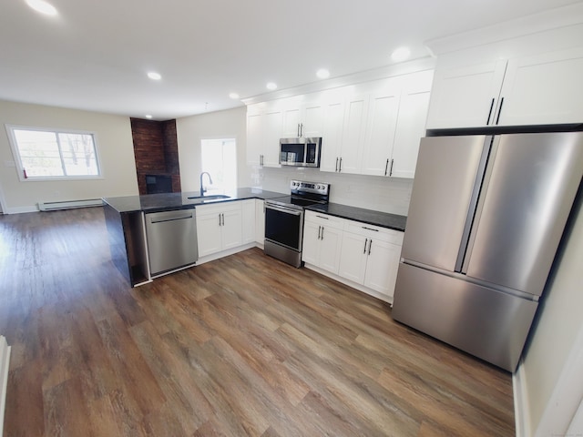 kitchen featuring white cabinetry, a sink, appliances with stainless steel finishes, dark countertops, and baseboard heating