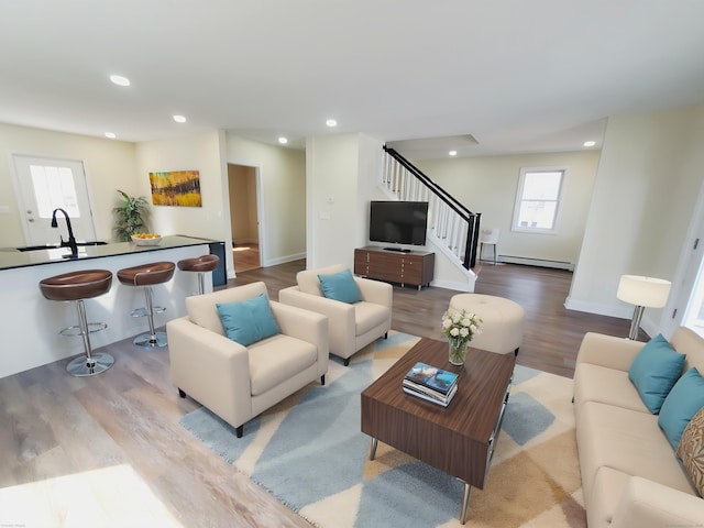 living area with baseboard heating, stairway, wood finished floors, and recessed lighting