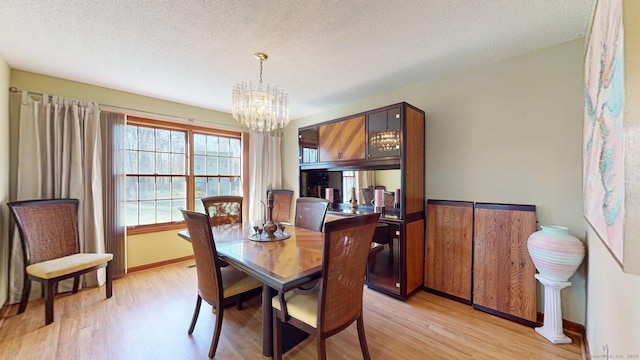 dining space featuring light wood-style flooring, a textured ceiling, an inviting chandelier, and baseboards