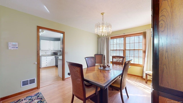 dining space featuring visible vents, baseboards, a chandelier, and light wood-style floors