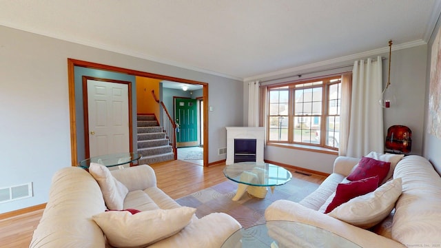 living area featuring crown molding, visible vents, light wood finished floors, and stairs