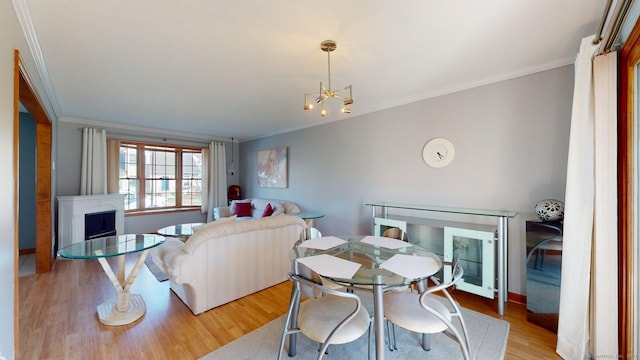 dining room with crown molding, an inviting chandelier, a fireplace, light wood finished floors, and baseboards