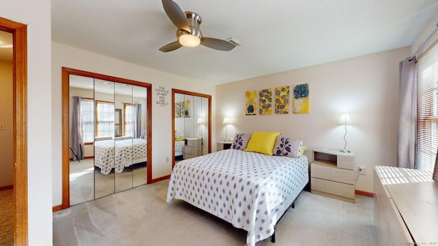 bedroom featuring visible vents, baseboards, two closets, ceiling fan, and light carpet