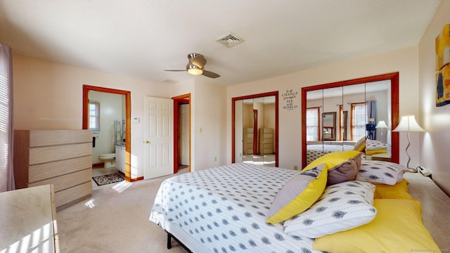 bedroom featuring visible vents, multiple closets, multiple windows, and light colored carpet