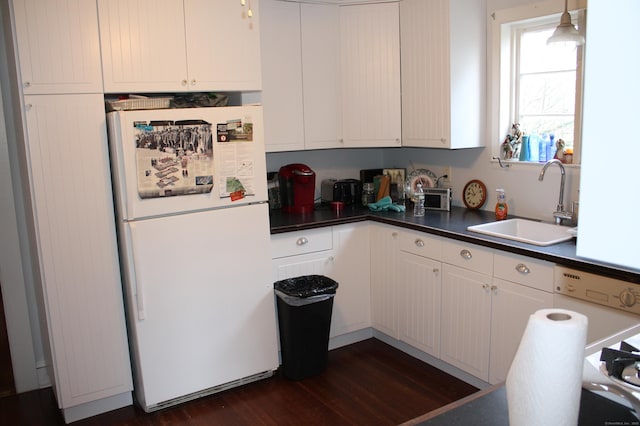 kitchen featuring a sink, dark countertops, white cabinets, freestanding refrigerator, and dark wood finished floors