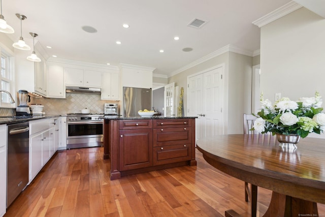 kitchen with ornamental molding, light wood-style floors, under cabinet range hood, stainless steel appliances, and decorative backsplash