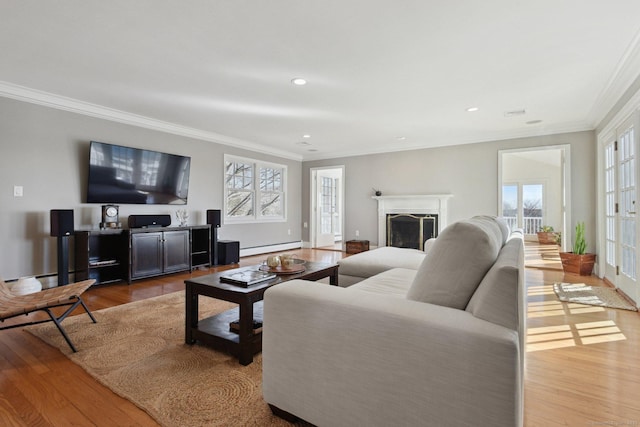 living room with a wealth of natural light, baseboard heating, ornamental molding, and wood finished floors