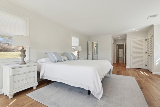 bedroom with multiple closets, visible vents, crown molding, and wood finished floors
