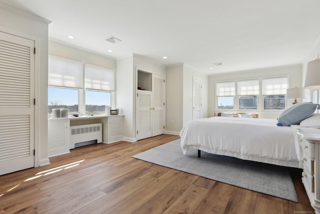 bedroom featuring hardwood / wood-style floors, multiple closets, radiator, and crown molding