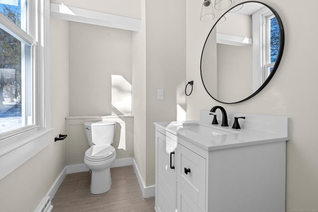 half bath with baseboards, toilet, a baseboard radiator, vanity, and wood finished floors