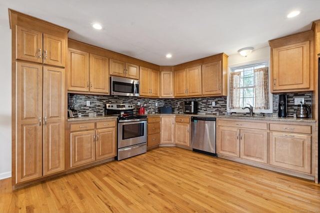 kitchen featuring light wood-type flooring, stainless steel appliances, a sink, and backsplash