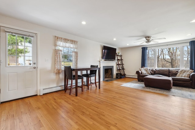 living area with a baseboard heating unit, a fireplace with flush hearth, light wood-style floors, and recessed lighting