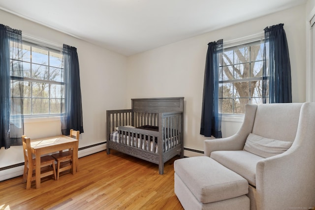bedroom featuring a baseboard heating unit, a crib, and light wood-style floors
