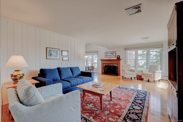 living area featuring a brick fireplace, visible vents, a baseboard radiator, and light wood-style floors