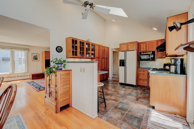 kitchen with black microwave, white refrigerator with ice dispenser, decorative backsplash, under cabinet range hood, and a skylight