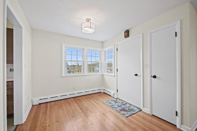 interior space with a baseboard heating unit, baseboards, and light wood-style flooring