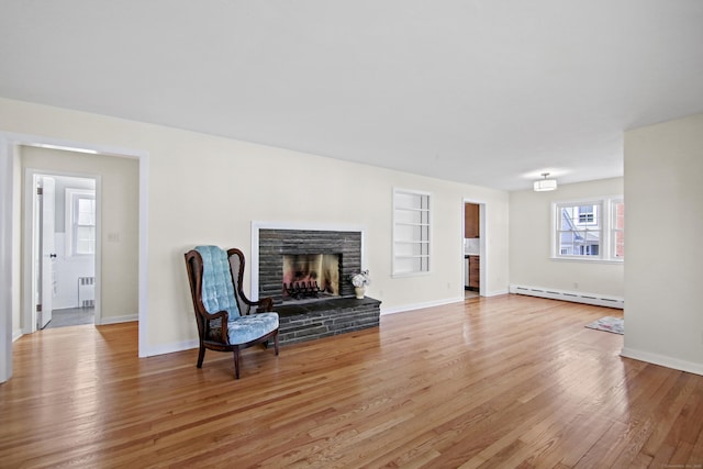 living area featuring radiator heating unit, a fireplace with raised hearth, a baseboard heating unit, light wood-type flooring, and baseboards