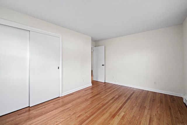 unfurnished bedroom featuring light wood-type flooring, baseboards, and a closet