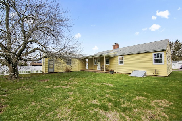 rear view of house with covered porch, a lawn, a chimney, and fence