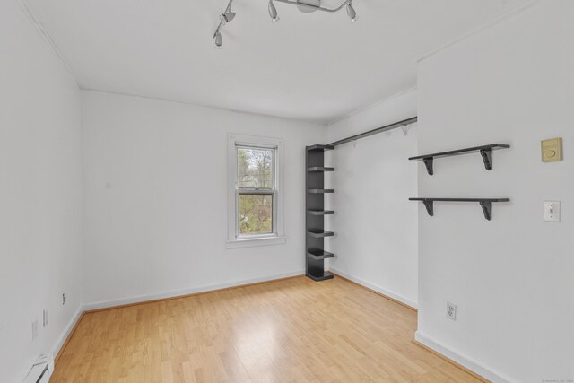 empty room with baseboards, track lighting, wood finished floors, and a baseboard radiator