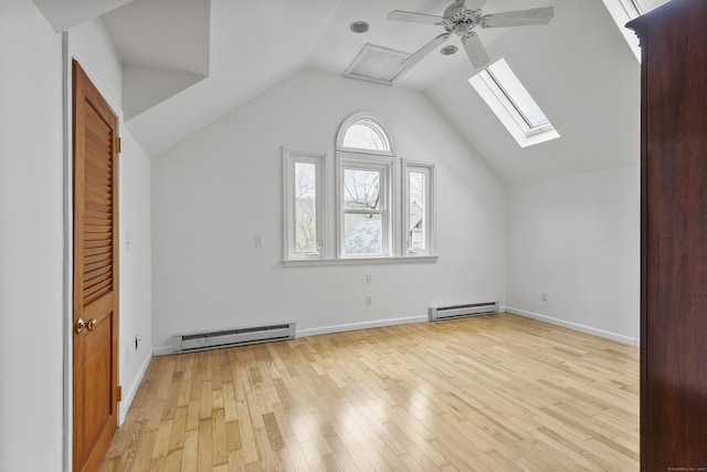 additional living space with ceiling fan, a baseboard heating unit, vaulted ceiling with skylight, and light wood-type flooring