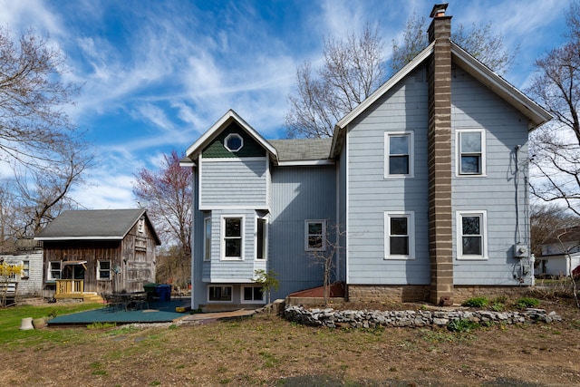 rear view of house with a chimney, an outdoor structure, and a patio area