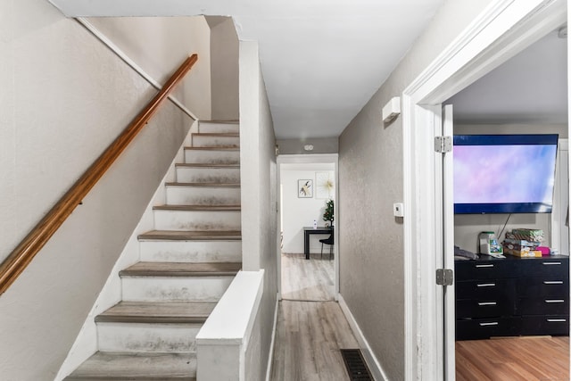 staircase with visible vents, a textured wall, and wood finished floors