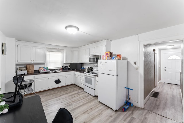 kitchen featuring light wood-style flooring, a sink, dark countertops, and white appliances