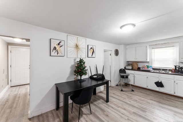 interior space featuring light wood-style floors, white cabinetry, a sink, dark countertops, and baseboards