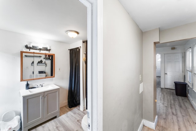 corridor featuring light wood-style flooring, a sink, and baseboards