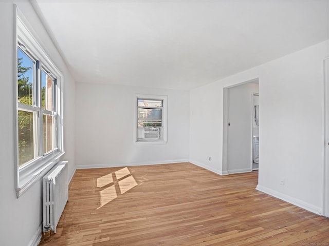 empty room with radiator, baseboards, and light wood finished floors