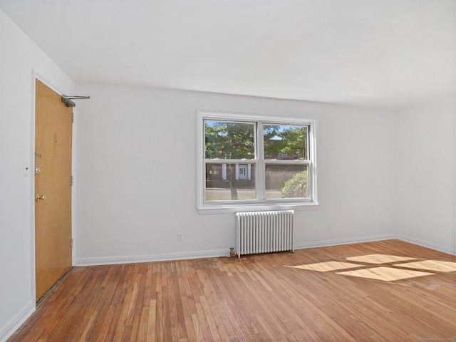 unfurnished room with baseboards, radiator heating unit, and hardwood / wood-style floors