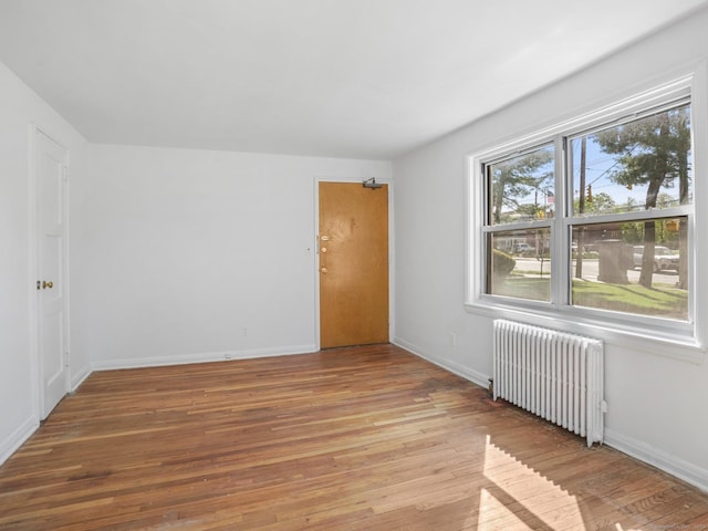 unfurnished room with baseboards, radiator, and light wood-type flooring