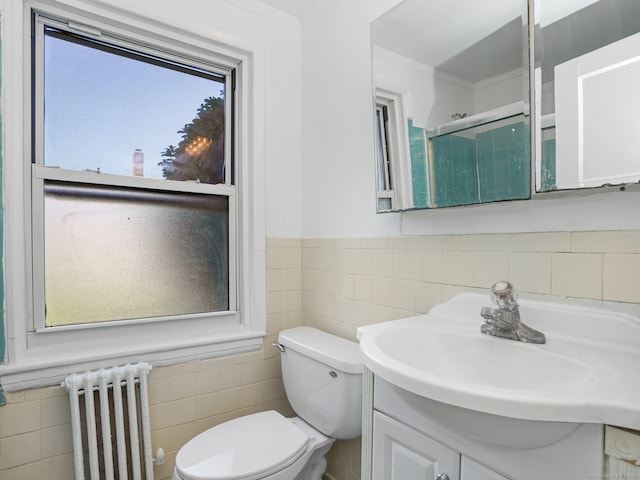 bathroom with a shower with shower door, vanity, toilet, radiator, and tile walls