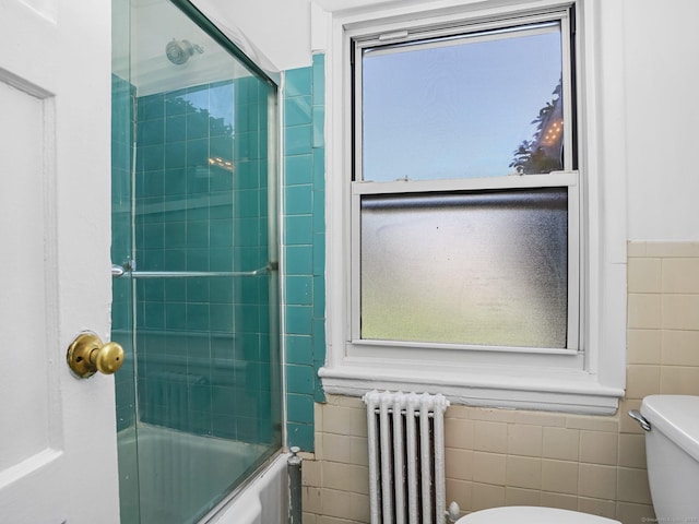 bathroom featuring radiator, wainscoting, shower / bath combination with glass door, toilet, and tile walls