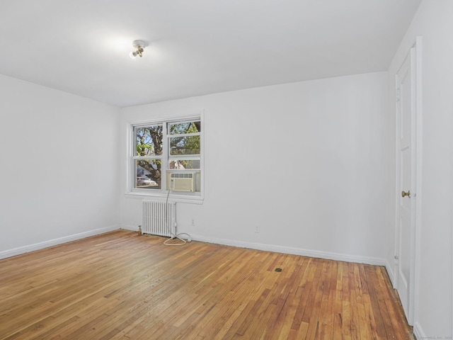 spare room featuring light wood-style floors, baseboards, radiator heating unit, and cooling unit