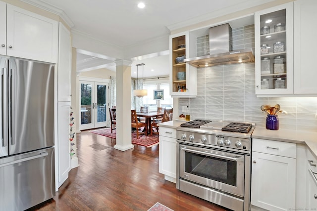 kitchen featuring stainless steel appliances, light countertops, glass insert cabinets, wall chimney exhaust hood, and tasteful backsplash