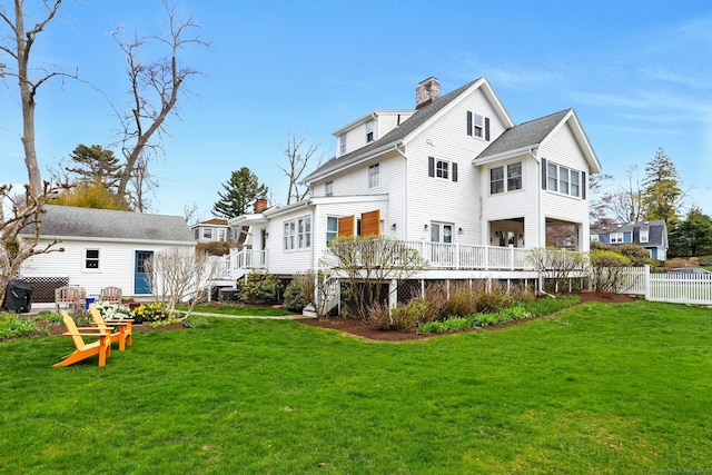 rear view of house featuring a chimney, fence, a deck, and a lawn