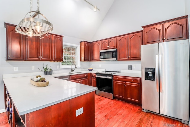kitchen featuring a peninsula, light countertops, light wood-style floors, stainless steel appliances, and a sink